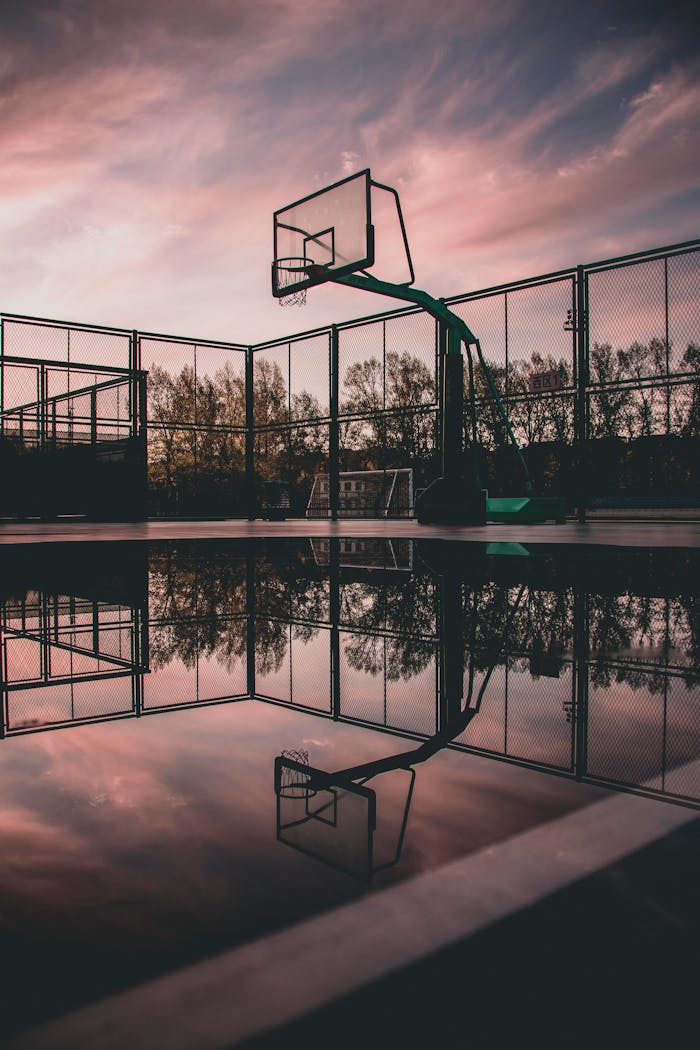 Home A tranquil view of a basketball court with reflections during sunset, creating a serene urban landscape.
