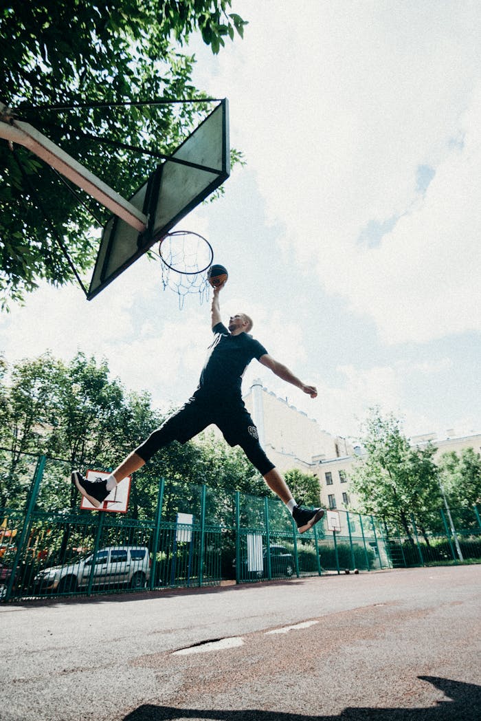 A skilled player performs a basketball dunk on an outdoor court under a clear sky.